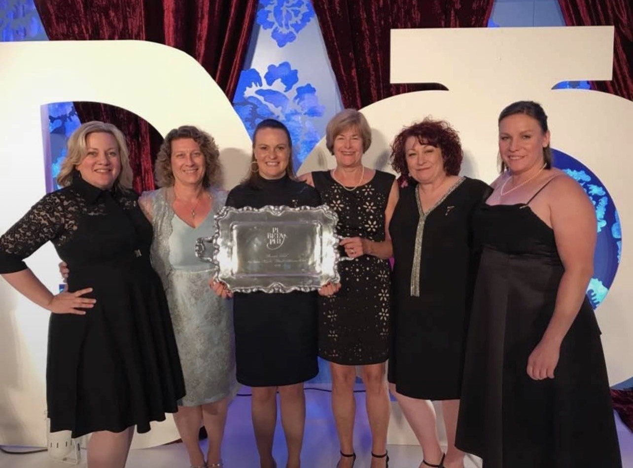 Several people posed indoors holding a plaque in front of large cutouts
