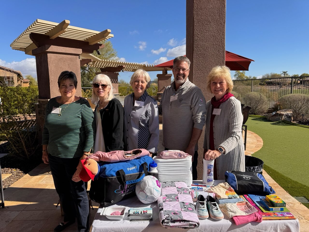 Four alumnae members and one gentleman standing outside behind a table filled with school supplies and sporting equipment