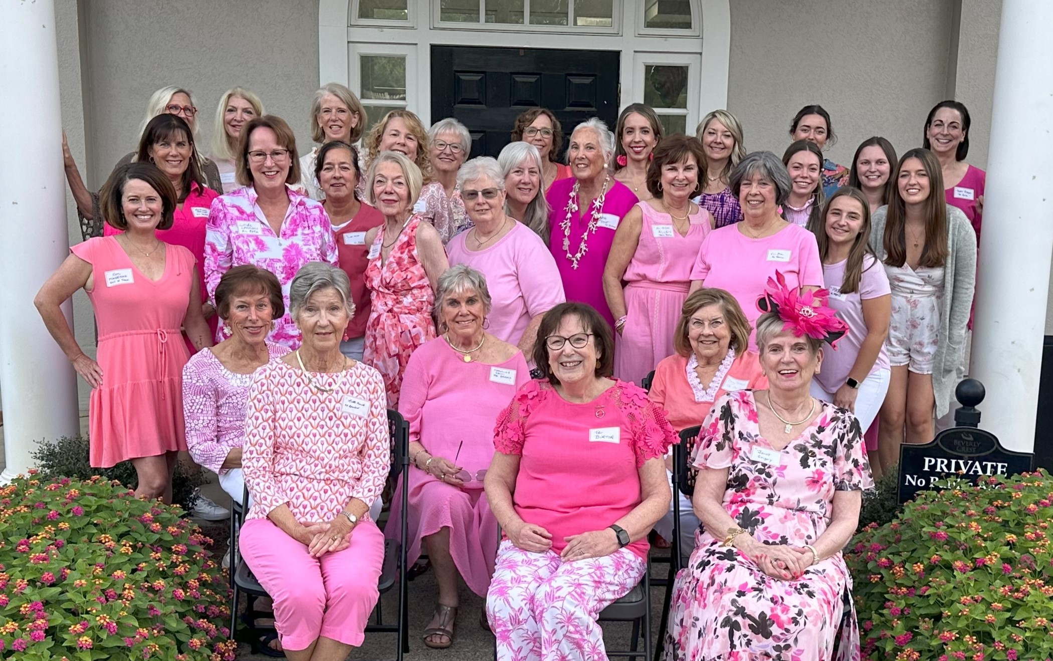 Several alumnae members wearing pink sitting and standing outside in front of a large house