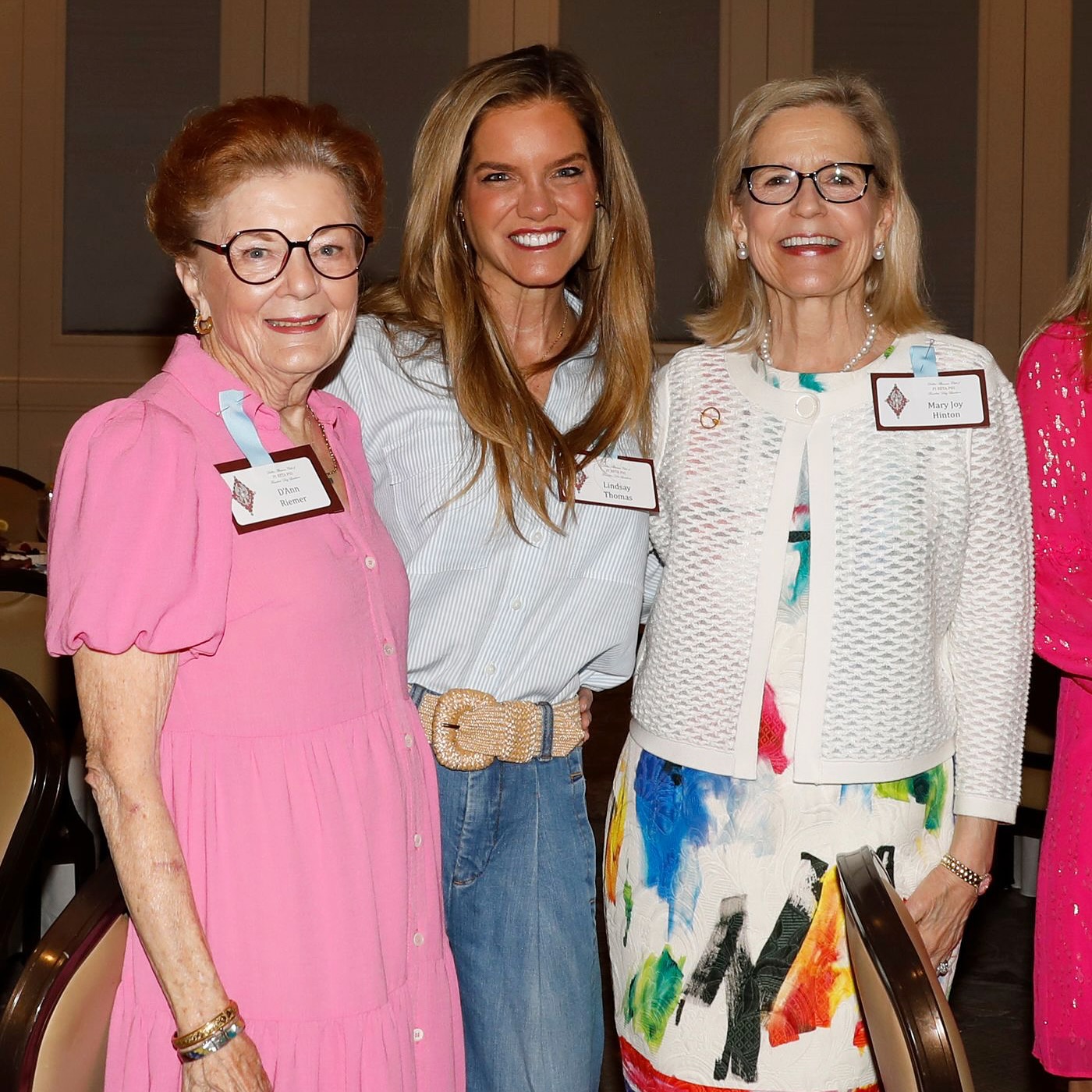 Three alumnae wearing a pink dress, white shirt and blue jeans and a colorful dress with a white cardigan standing indoors