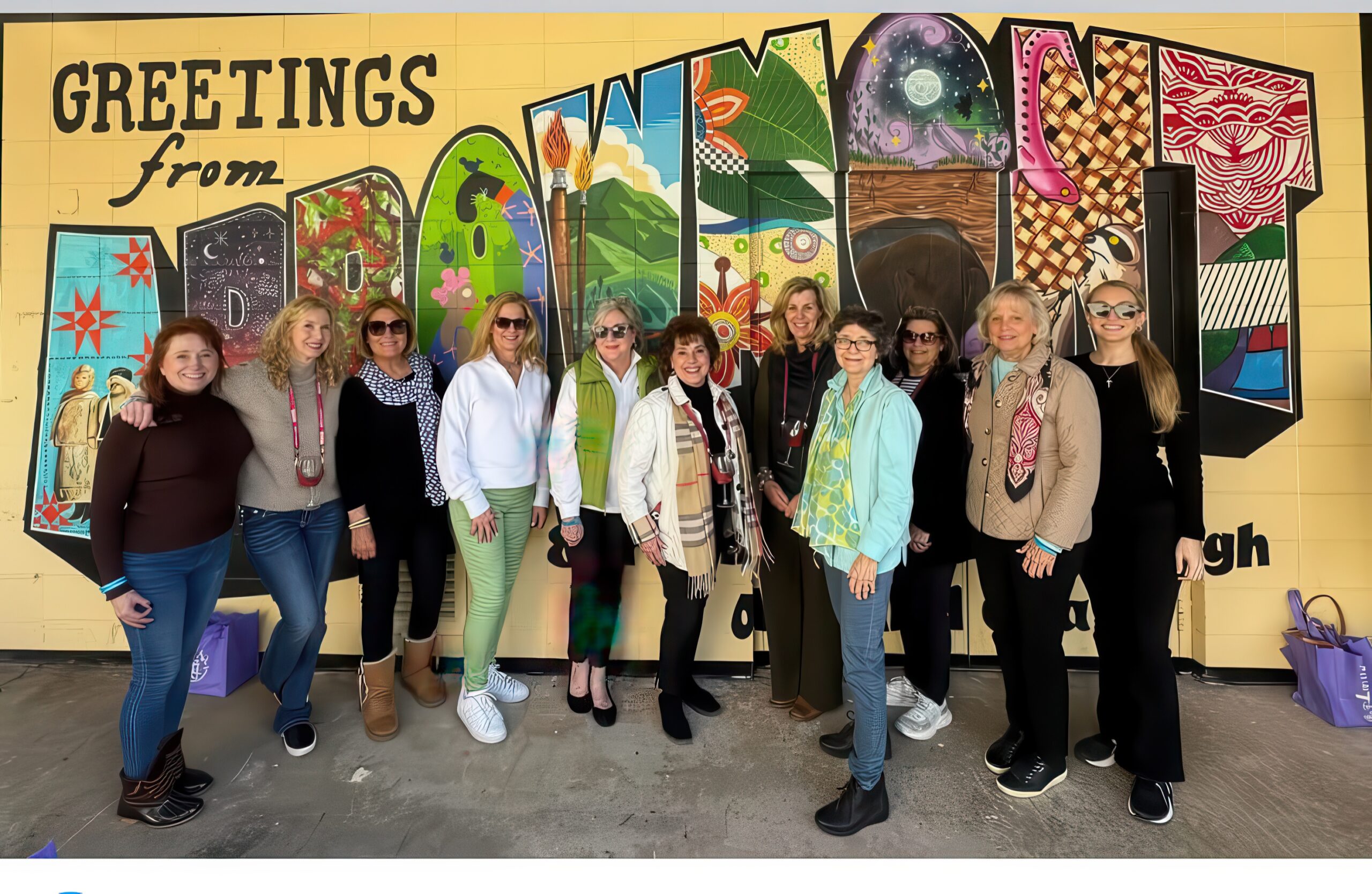 A group of members standing in front of a wall with a large mural that reads 