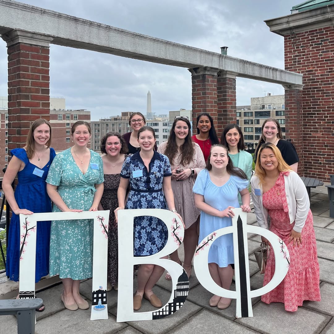 Several alumnae members in colorful dresses standing outside on a brick rooftop holding large white Pi Beta Phi Greek letters