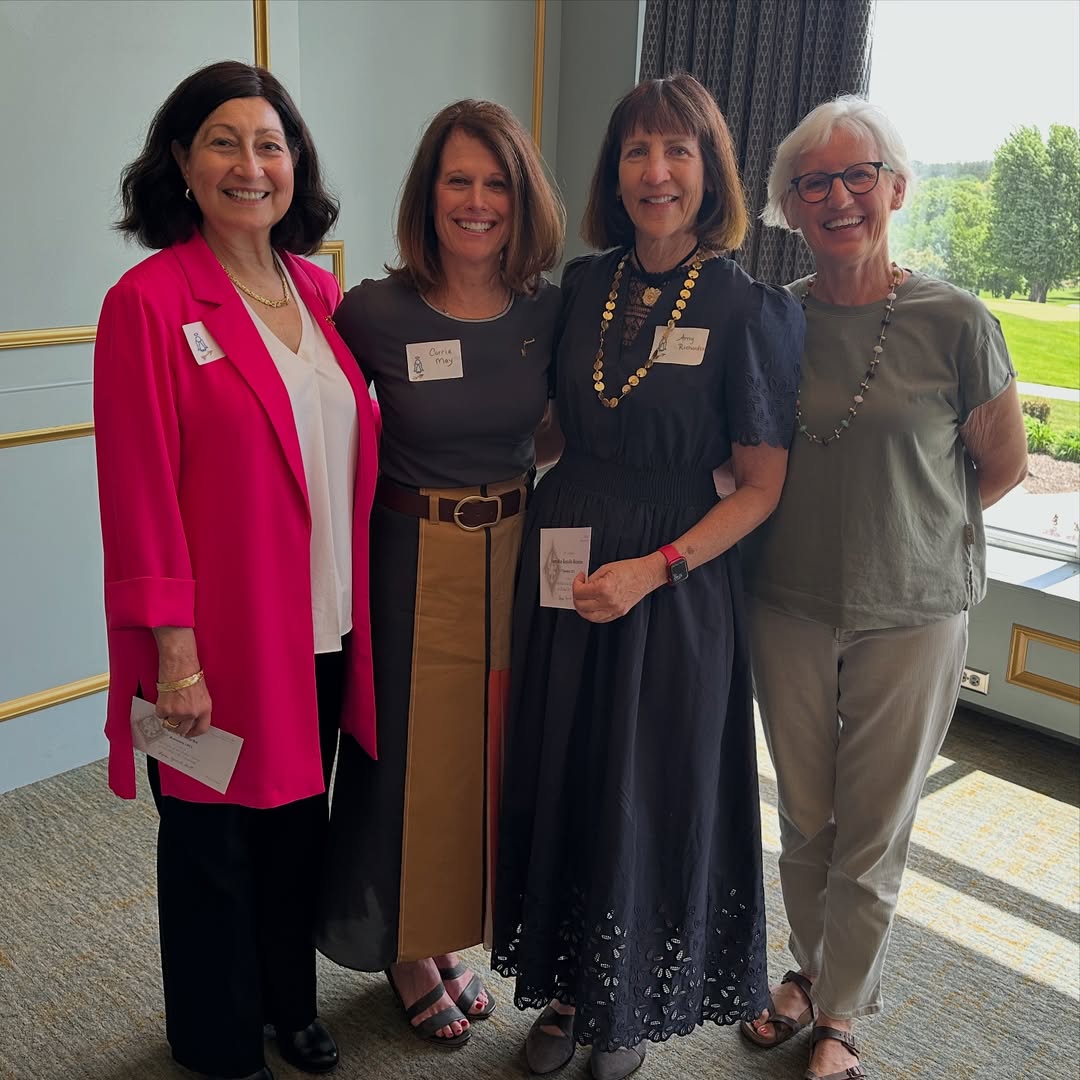 Four alumnae members wearing name tags standing inside in front of a window
