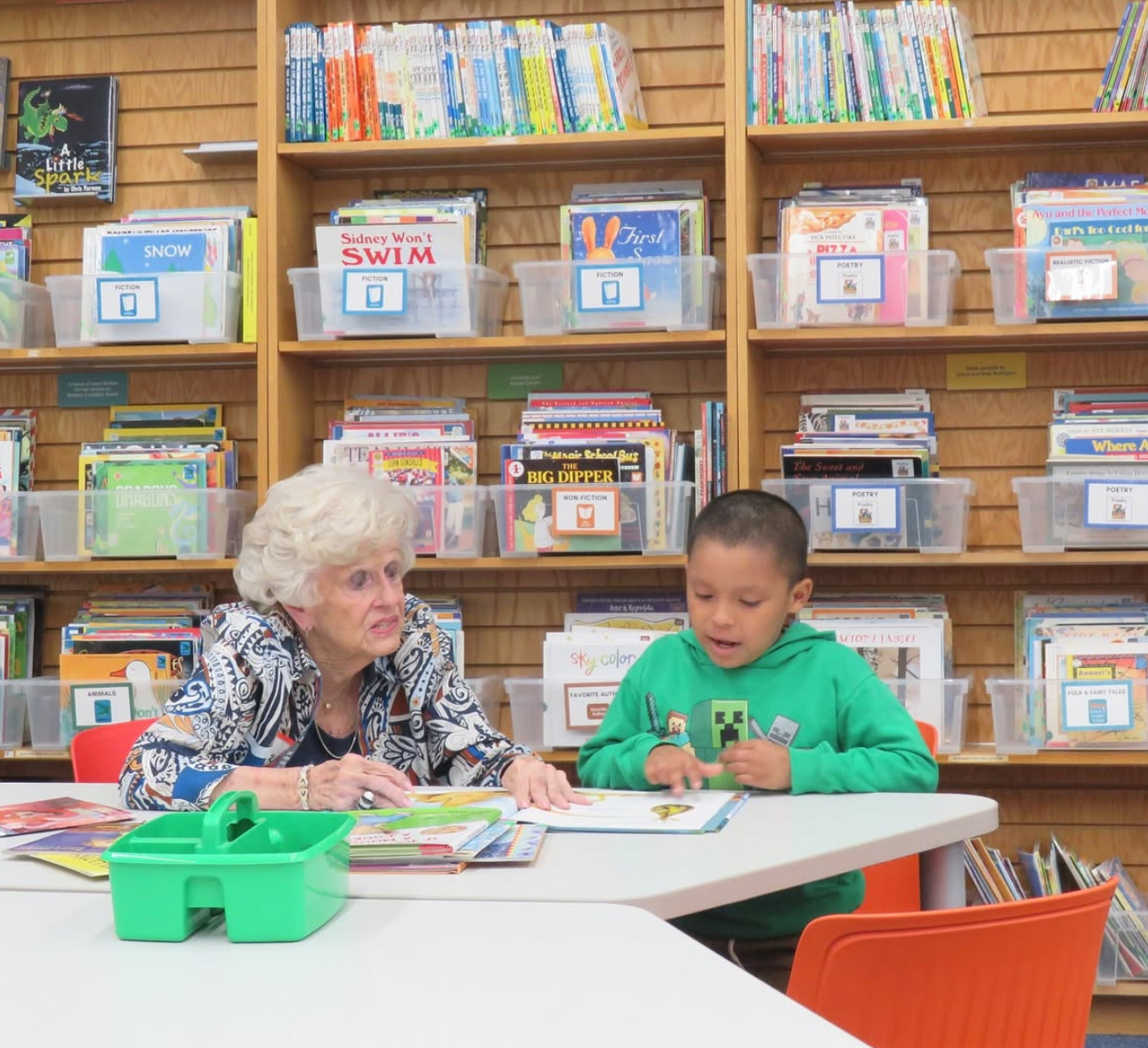 An older individual in a library reading with a child