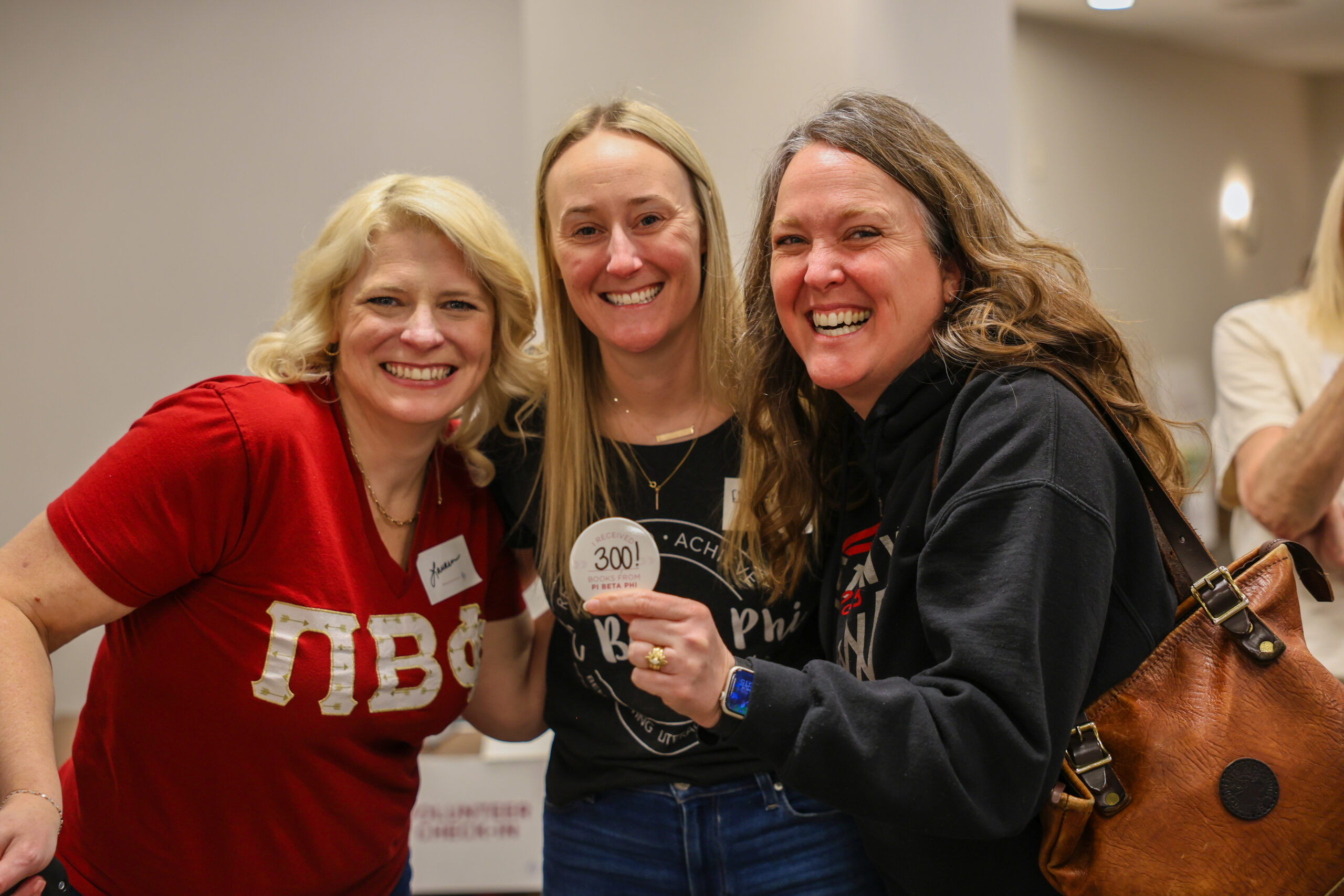 Three members standing together inside holding white buttons that read, "I received 300 books from Pi Beta Phi"