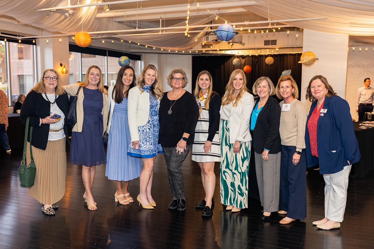 Several alumnae members standing inside with a paper solar system hanging from the ceiling