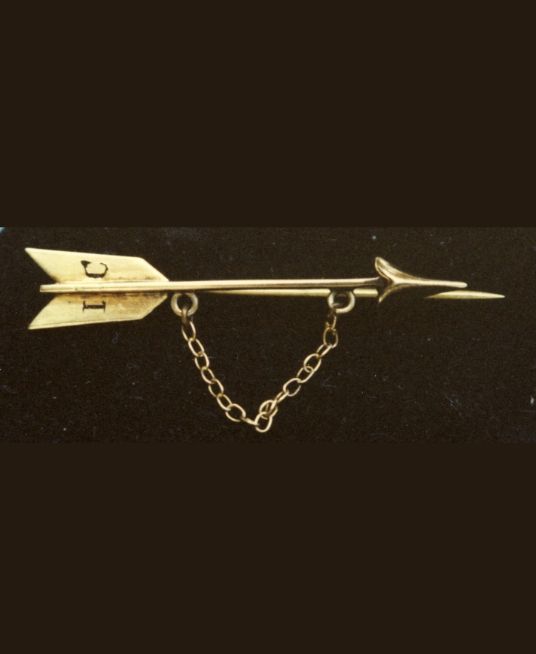 Close-up of a vintage Pi Beta Phi gold arrow pin with chain against a dark background