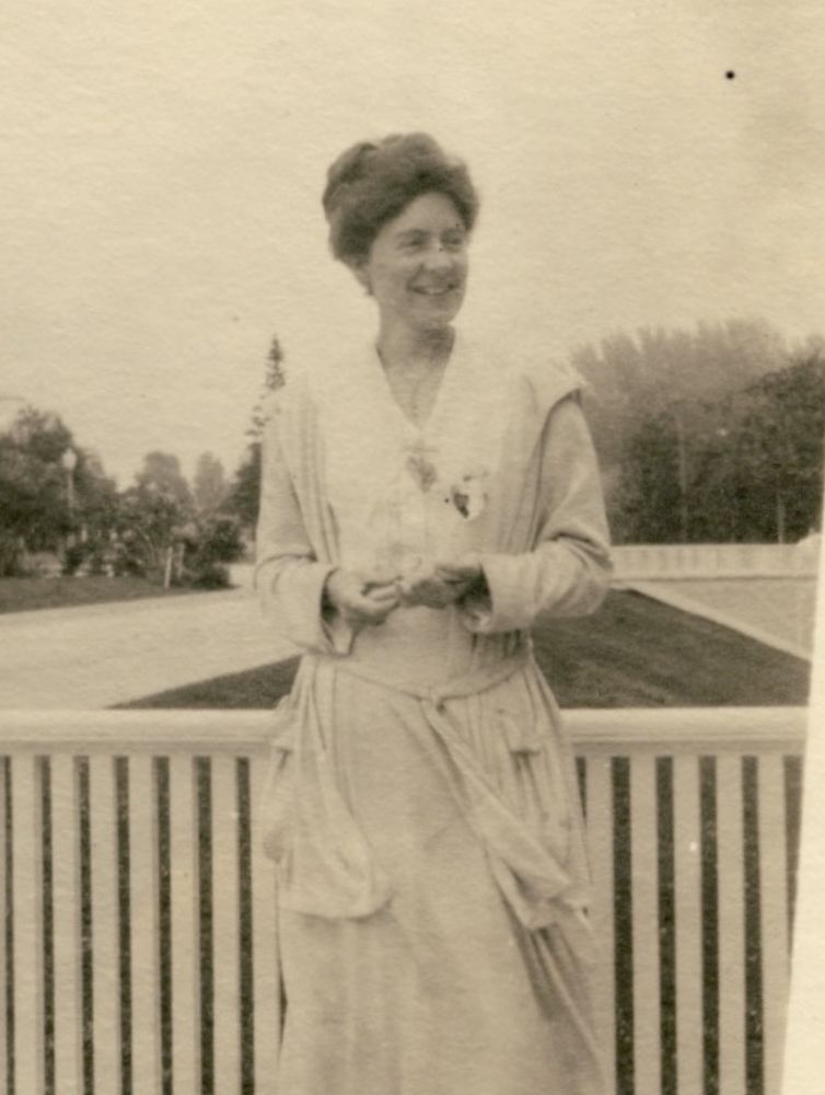 Sepia-toned historical photograph of a Pi Beta Phi member smiling on a porch in an Edwardian-era dress