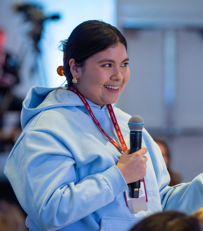 Pi Beta Phi member smiling and speaking into a microphone at an event while wearing a conference lanyard