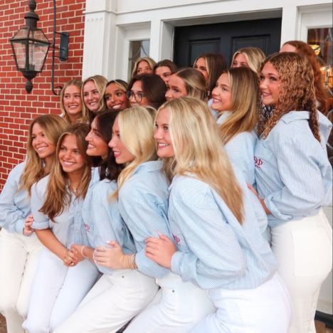 Group of Pi Beta Phi members smiling together on the steps of the chapter house at 1701, wearing matching light blue Pi Beta Phi button-down shirts and white pants