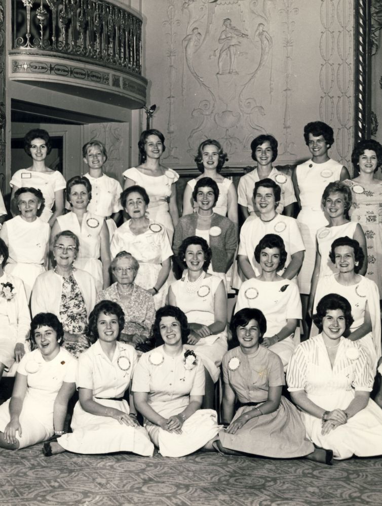 Black and white historical photograph of a large group of Pi Beta Phi members wearing name badges posed in rows inside an ornate ballroom in 1950s era clothing