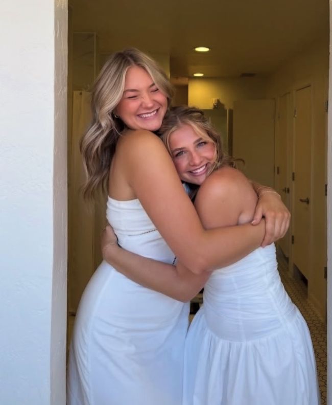 Two Pi Beta Phi members laughing and hugging in an arched doorway, both wearing white dresses at a recruitment event