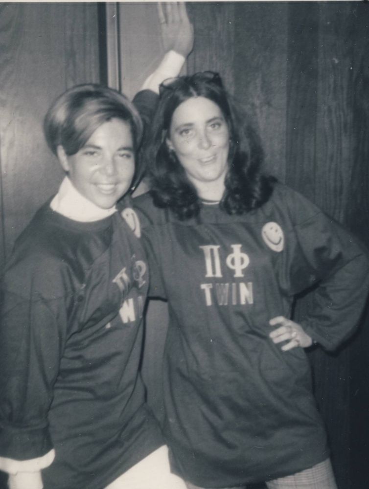 Black and white photo of two members standing close together wearing sweatshirts with Pi Phi Greek letters