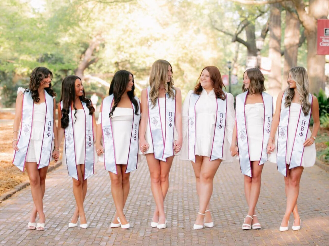 Seven members wearing graduation stoles and holding hands while looking at one another