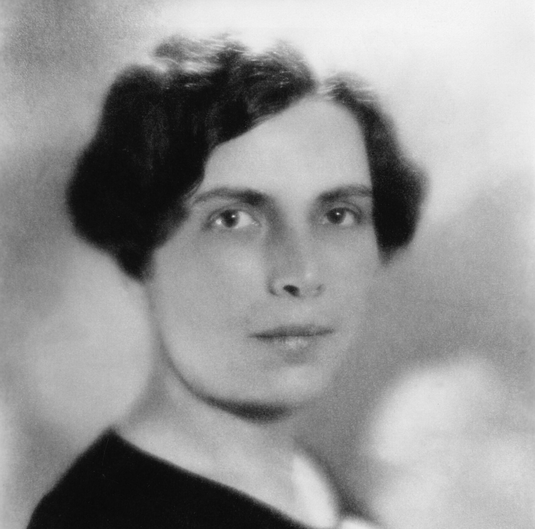 Historical black and white photo of Gladys Rowena Henry Dick wearing a black shirt in front of a greay background