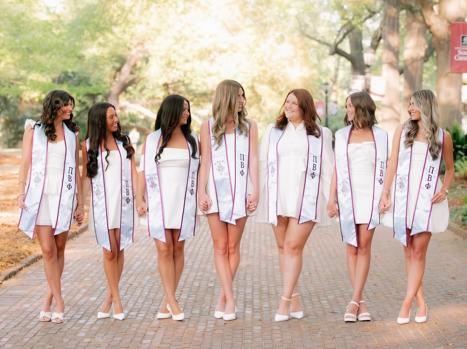 Seven members holding hands and looking at one another wearing graduation stoles