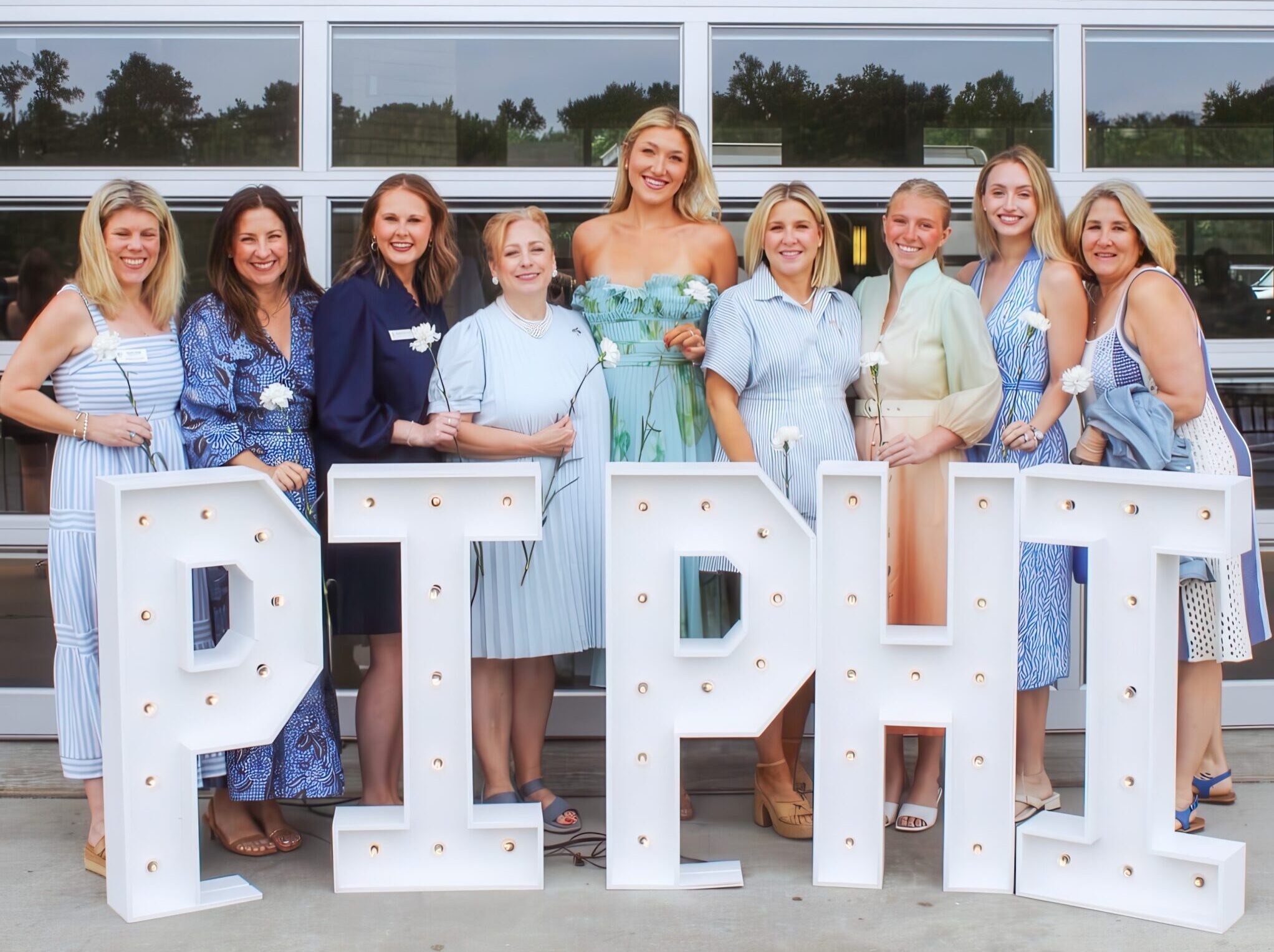 Nine individuals standing behind marquee letters that say Pi Phi