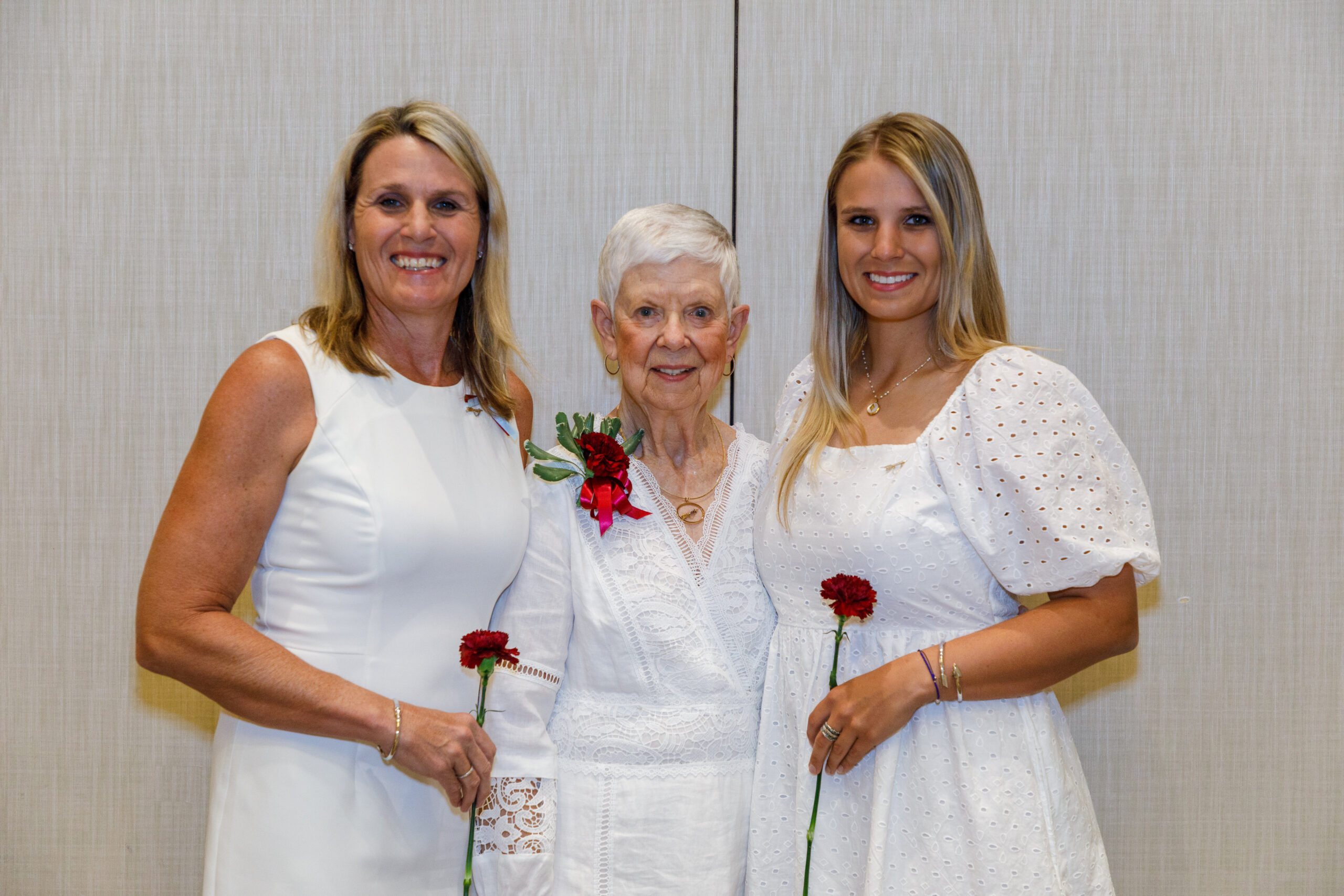 Three individuals wearing white and holding wine carnations