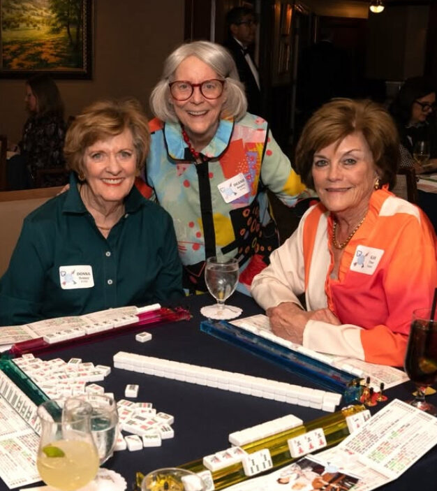 Two members sitting around a card table with one member leaning over them