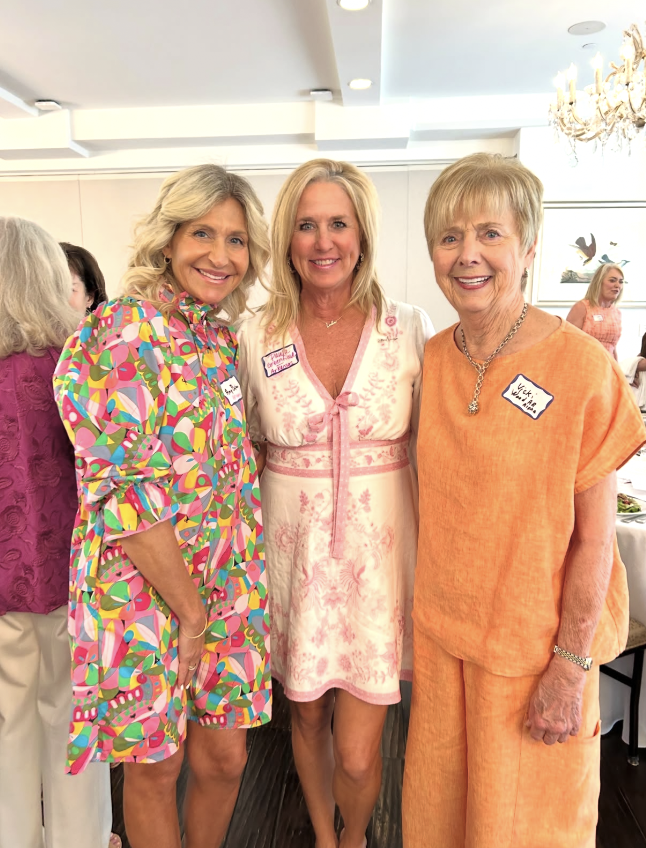 Three alumnae members in an orange, white and pink and colorful dress standing indoors
