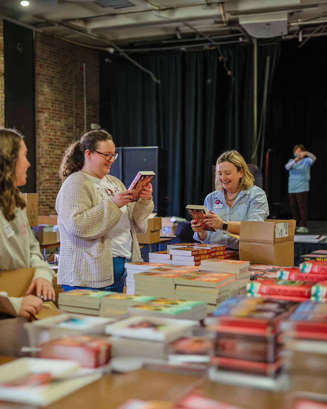 A group of people around a large stable with stack of colorful books on it