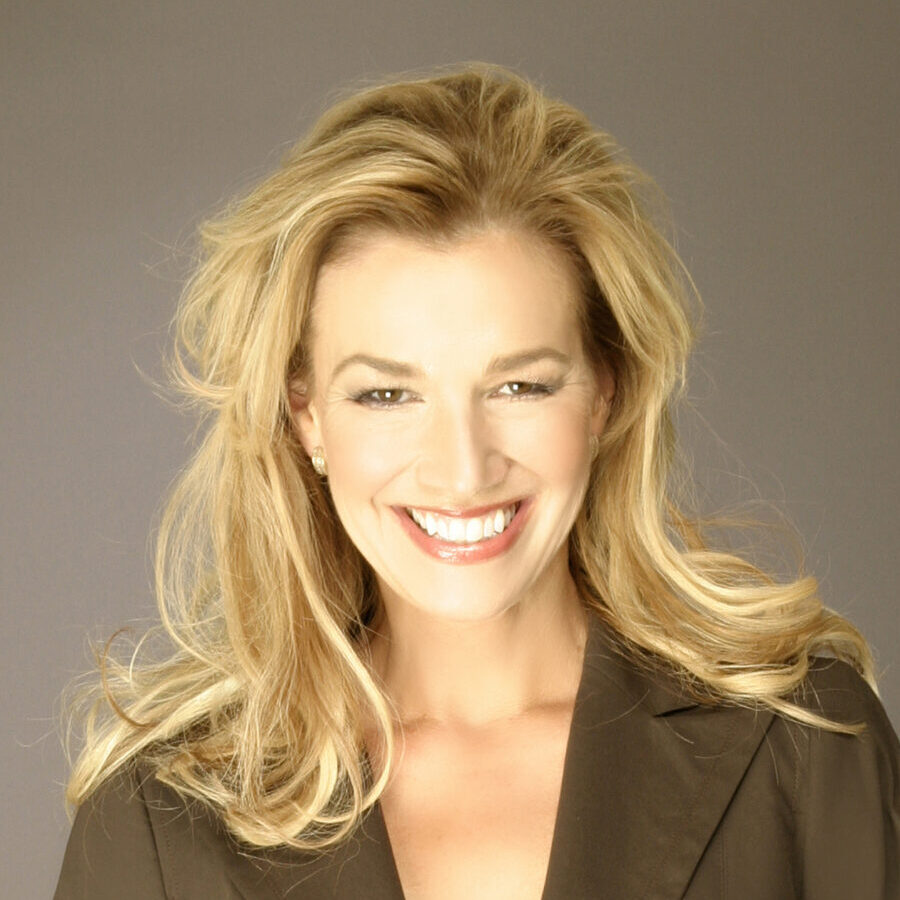 Professional headshot of Anne Bremner wearing a brown blazer in front of a brown background