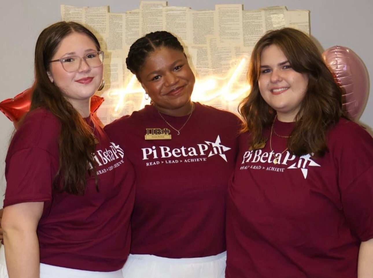 Three individuals standing indoors wearing matching shirts that say Pi Beta Phi