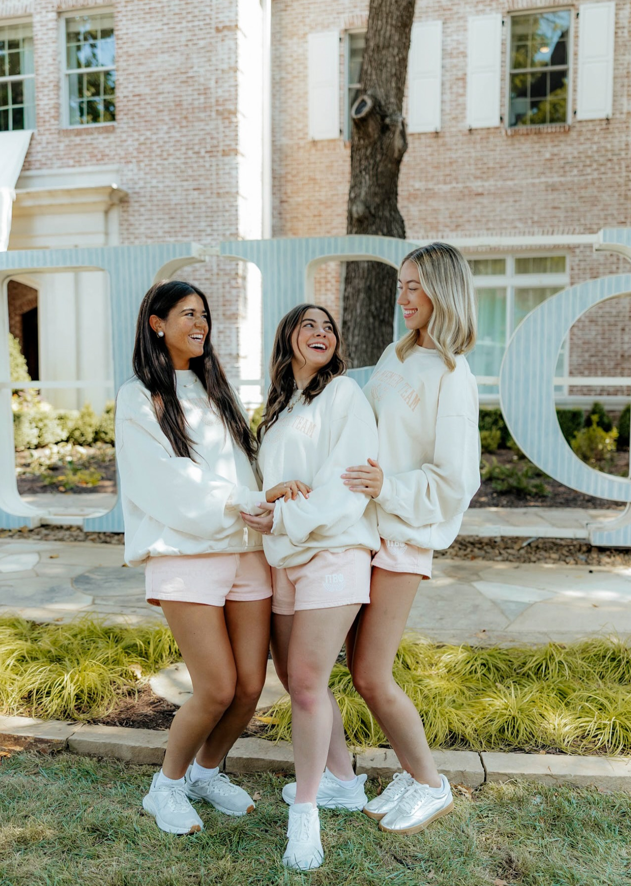 Three individuals standing outdoors in front of large wooden Pi Beta Phi greek letters