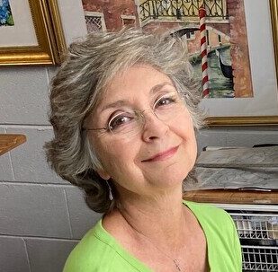 Headshot of Barbara Blanks Bullard wearing a lime green shirt standing in front of a white brick wall with picture frames on it