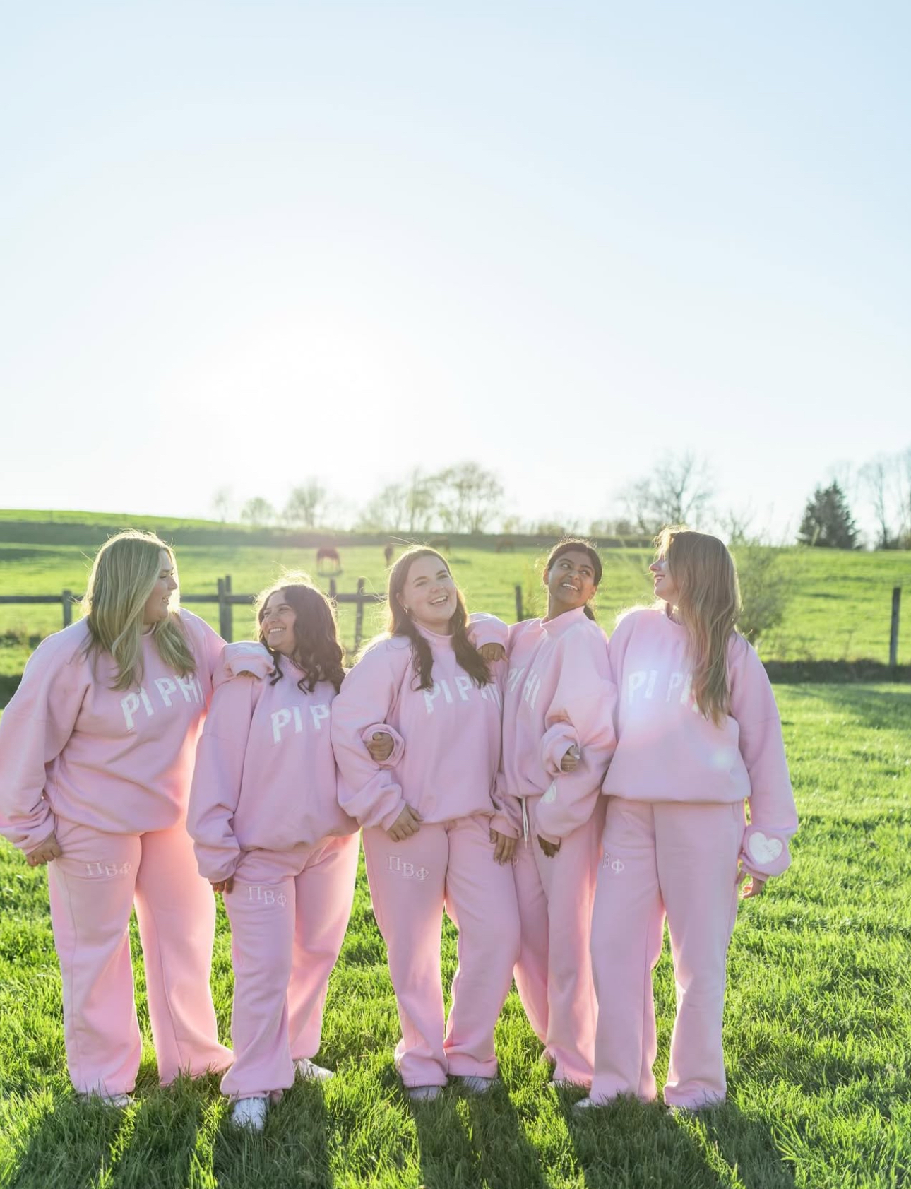 Five individuals standing outdoors in a grassy field wearing matching pink sweatsuits