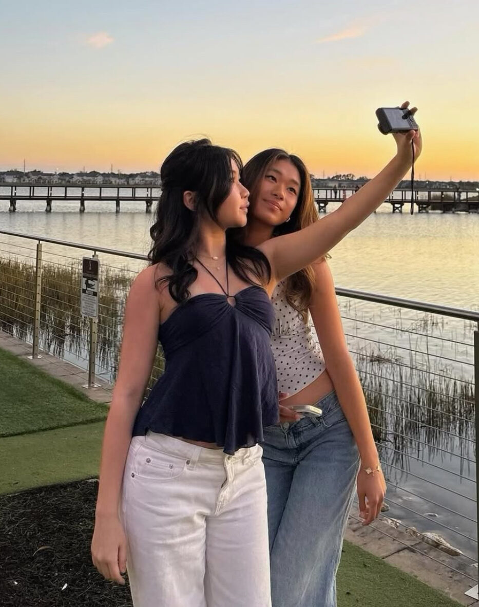 Two individuals taking a selfie in front of a lake