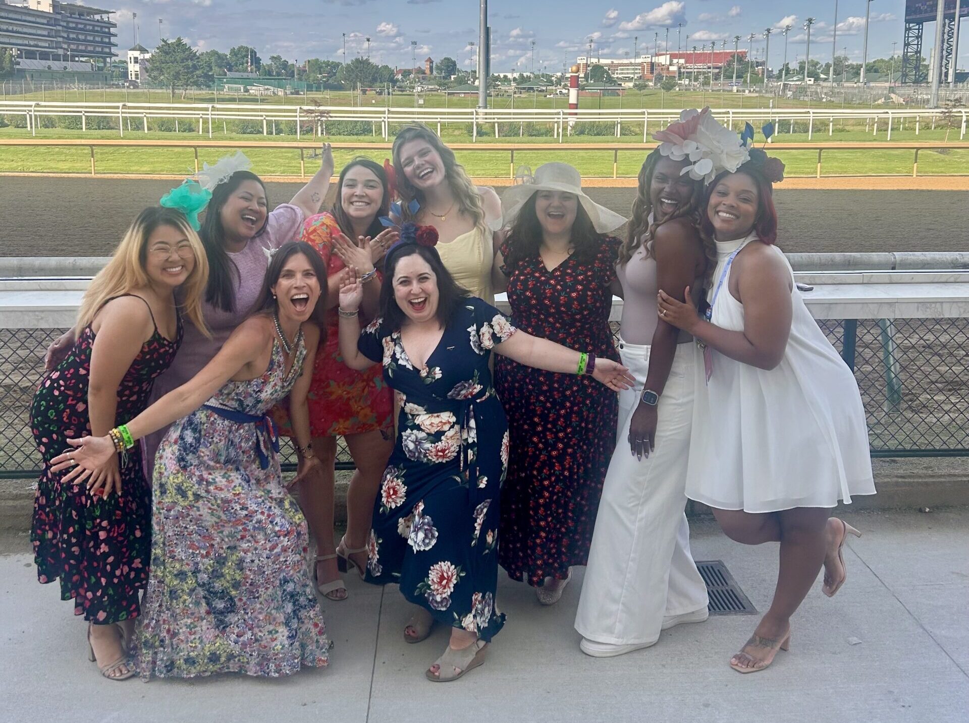 Several members wearing fascinator hats and headbands standing in front of a horse track