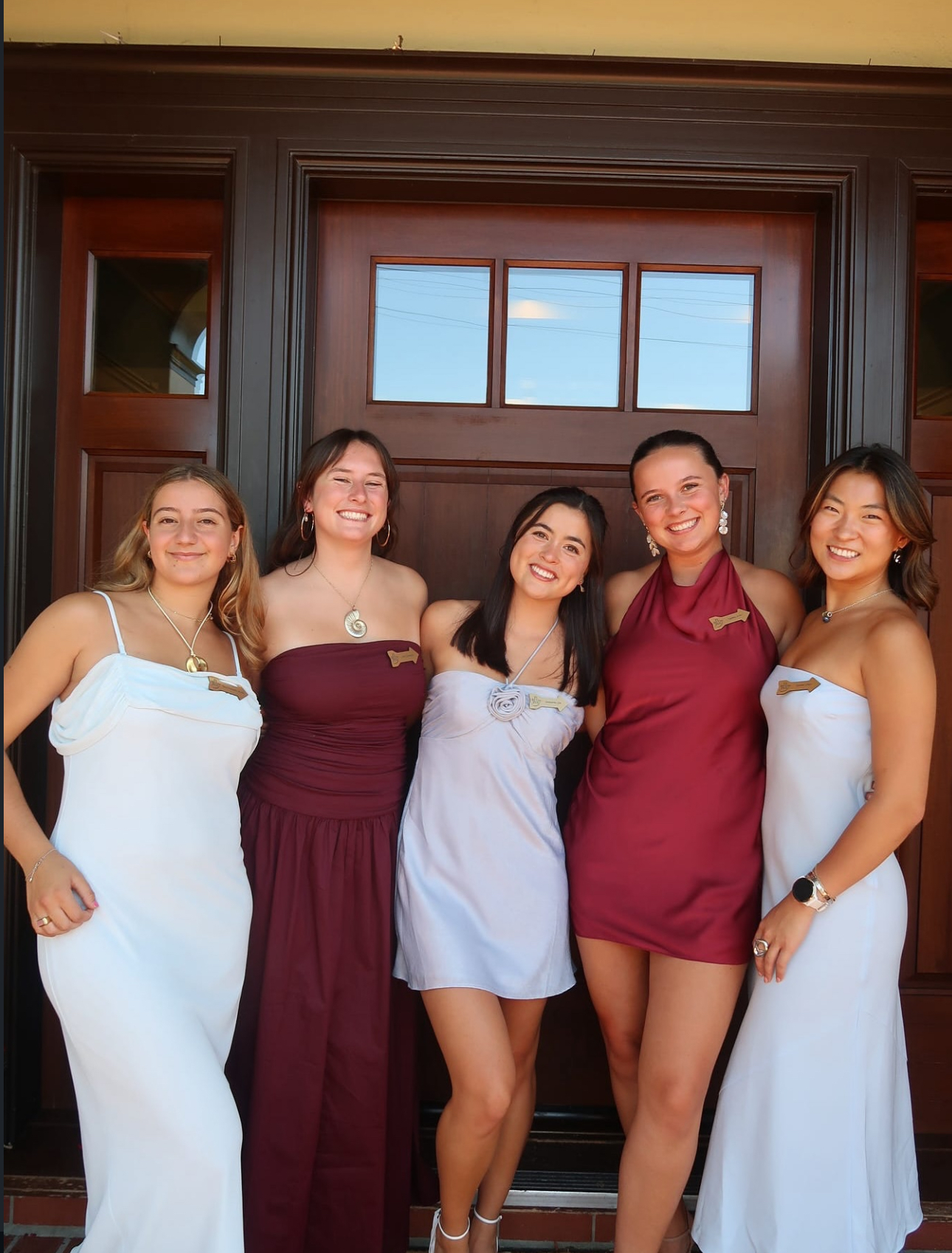 Five individuals standing in front of a doorway wearing wine and silver blue dresses