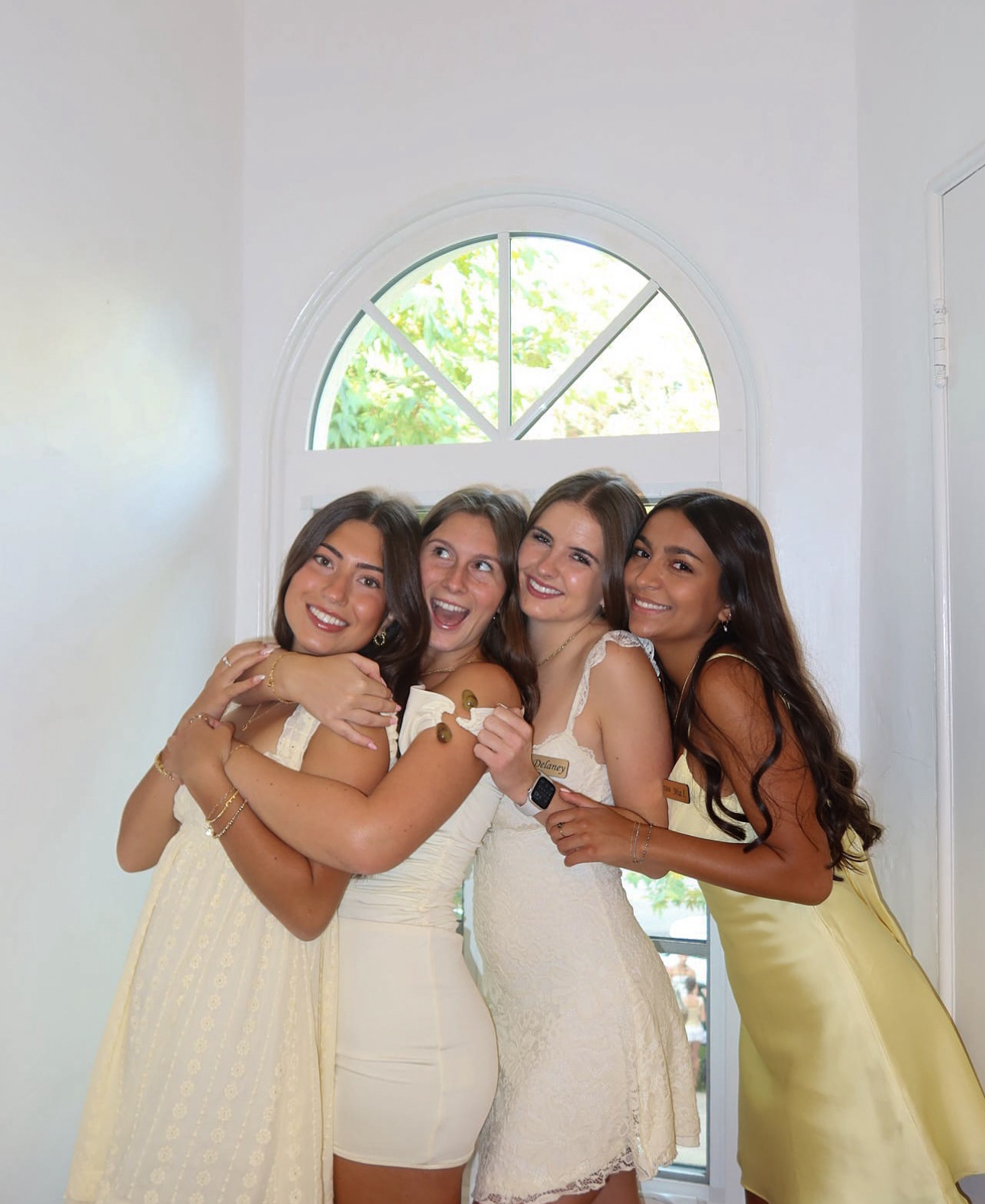 Four individuals wearing yellow dresses and hugging indoors
