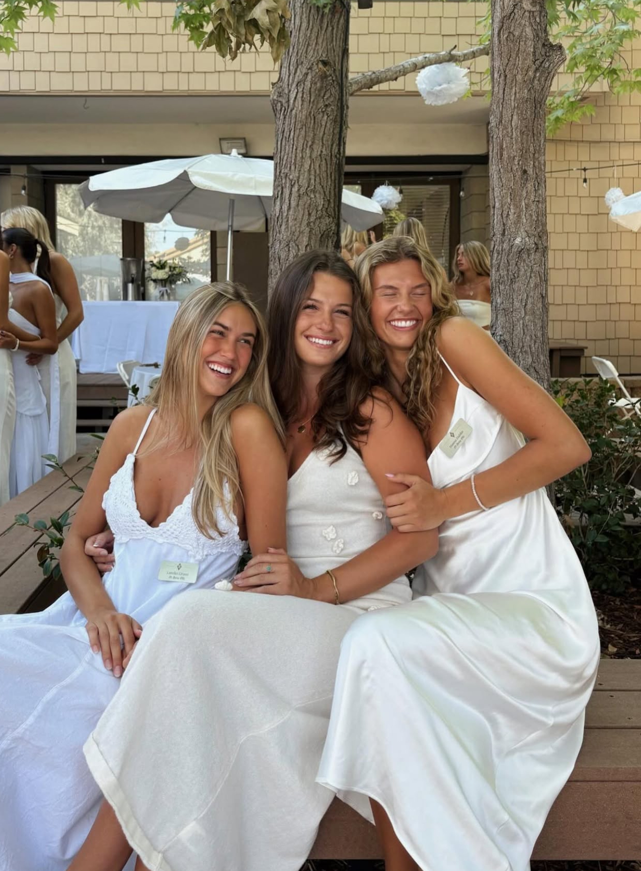 Three individuals wearing white dresses sitting outdoors