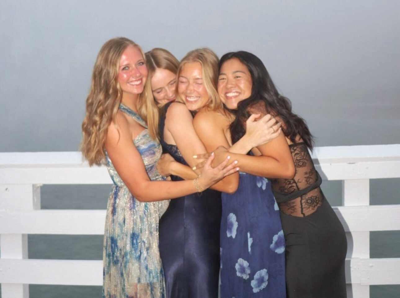 Four individuals standing outdoors hugging