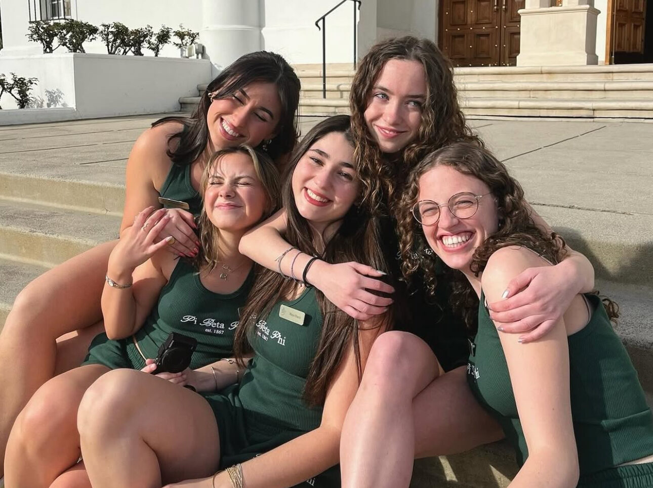 Five individuals sitting on stairs outdoors hugging