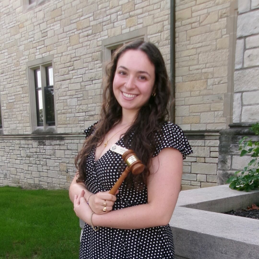 Professional headshot of Alia Beseio wearing a polka dot dress and holding a wooden gavel