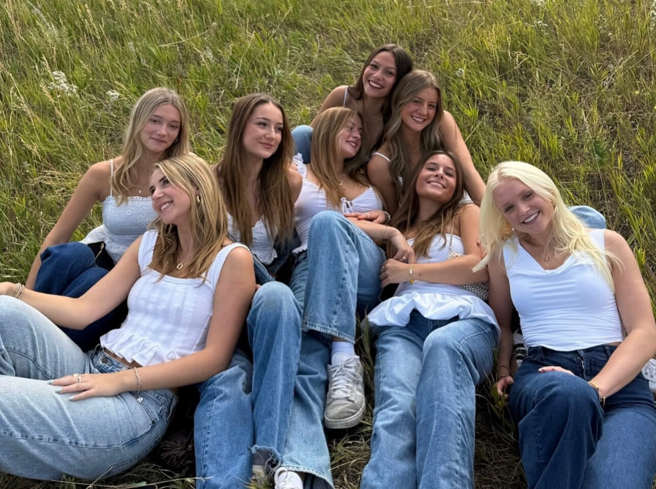 Eight individuals wearing white tops and jeans sitting in a field