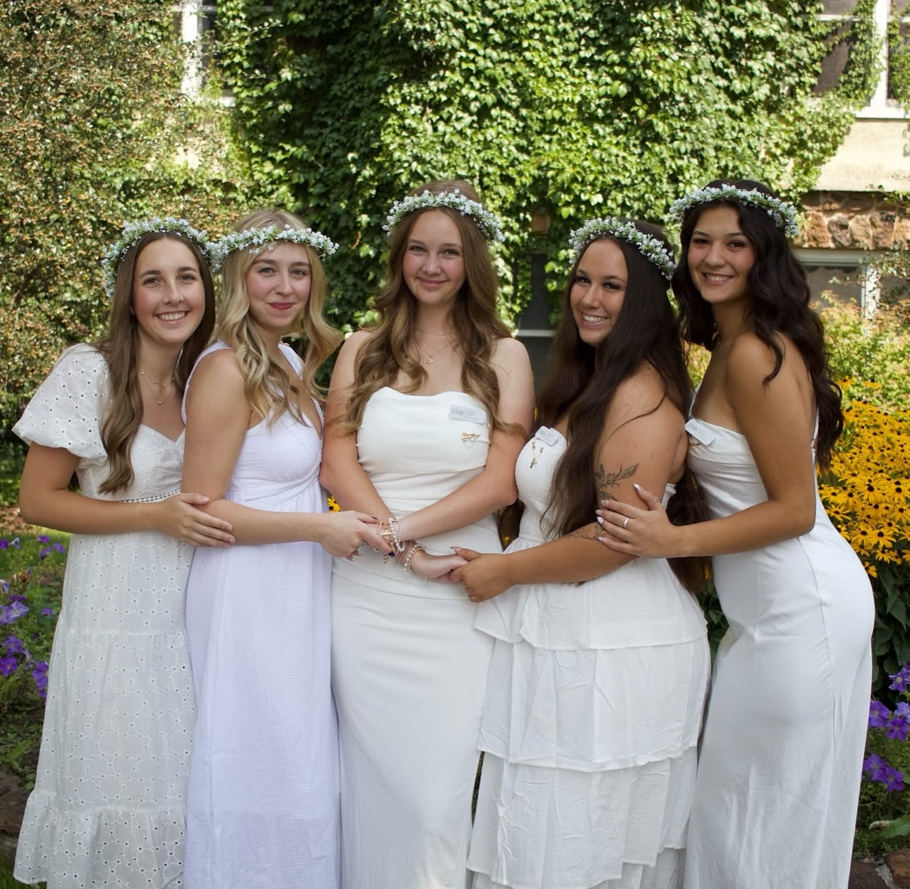 Five individuals wearing white dresses in front of a tree