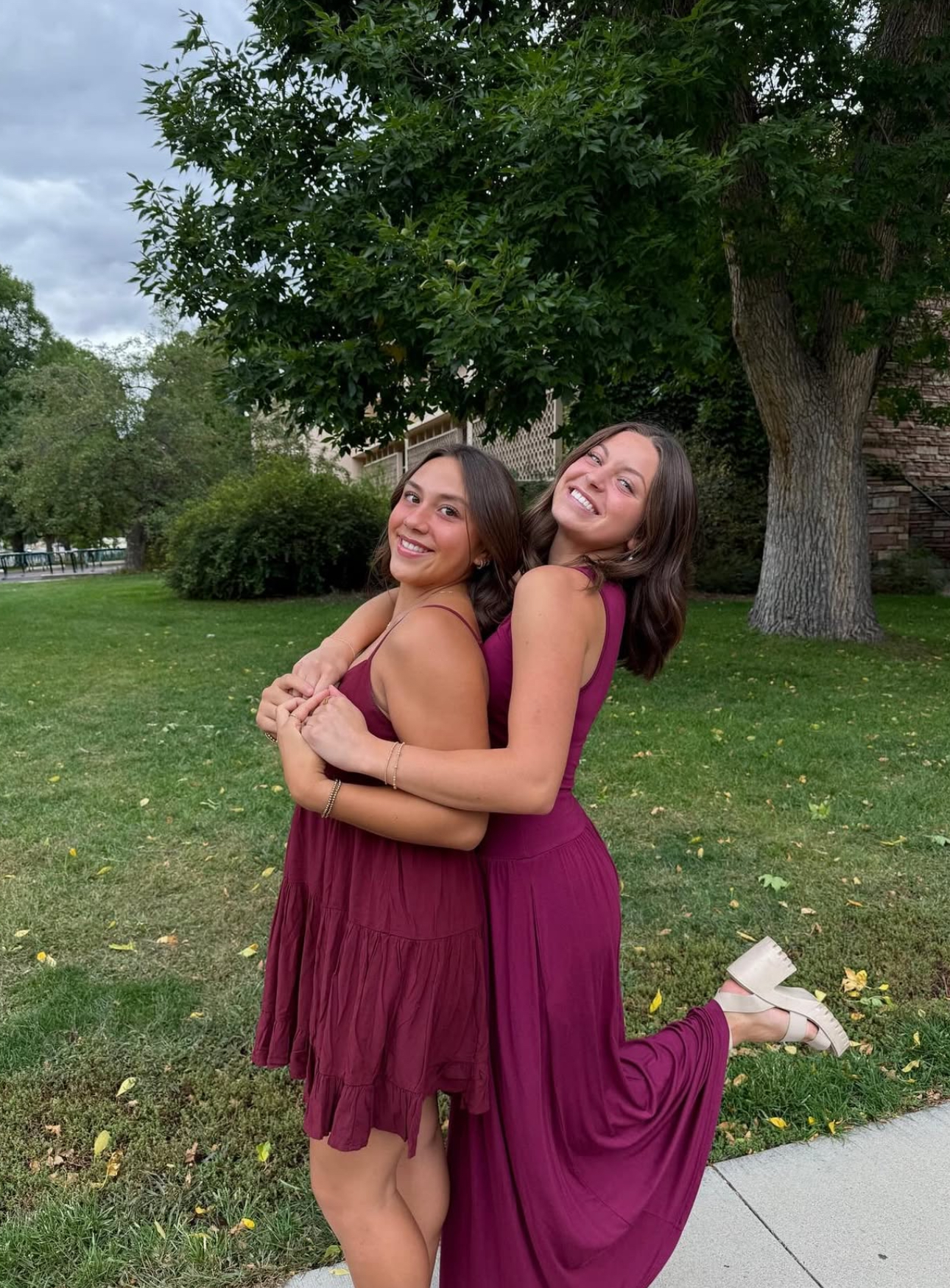 Two individuals wearing wine dresses standing on a patio hugging