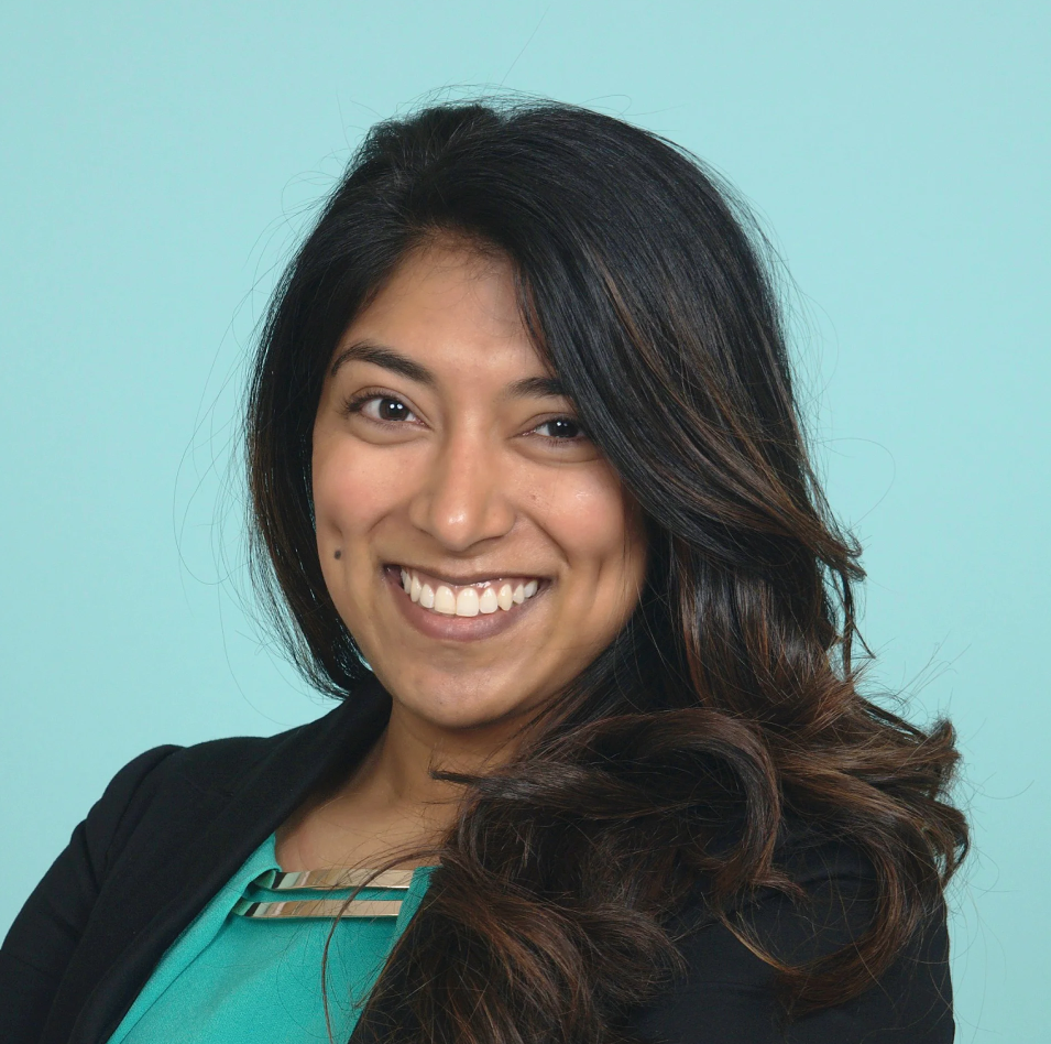 Professional headshot of Davina Durgana wearing a turquoise shirt and black blazer in front of a turquoise background