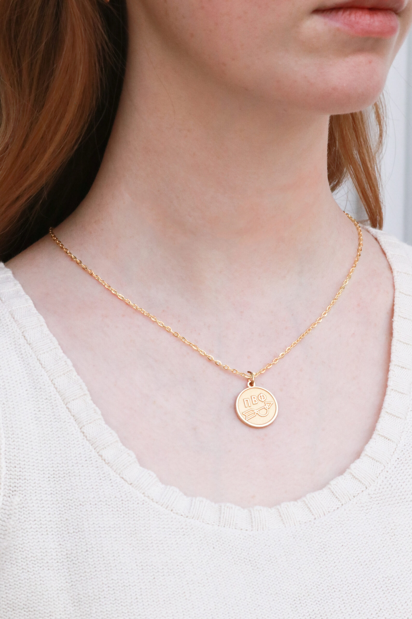 An individual wearing a gold necklace with a coin charm