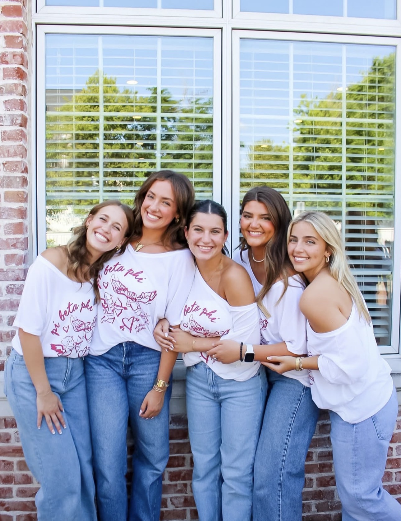 Five individuals standing in front of a window wearing matching white T-shirts and blue jeans