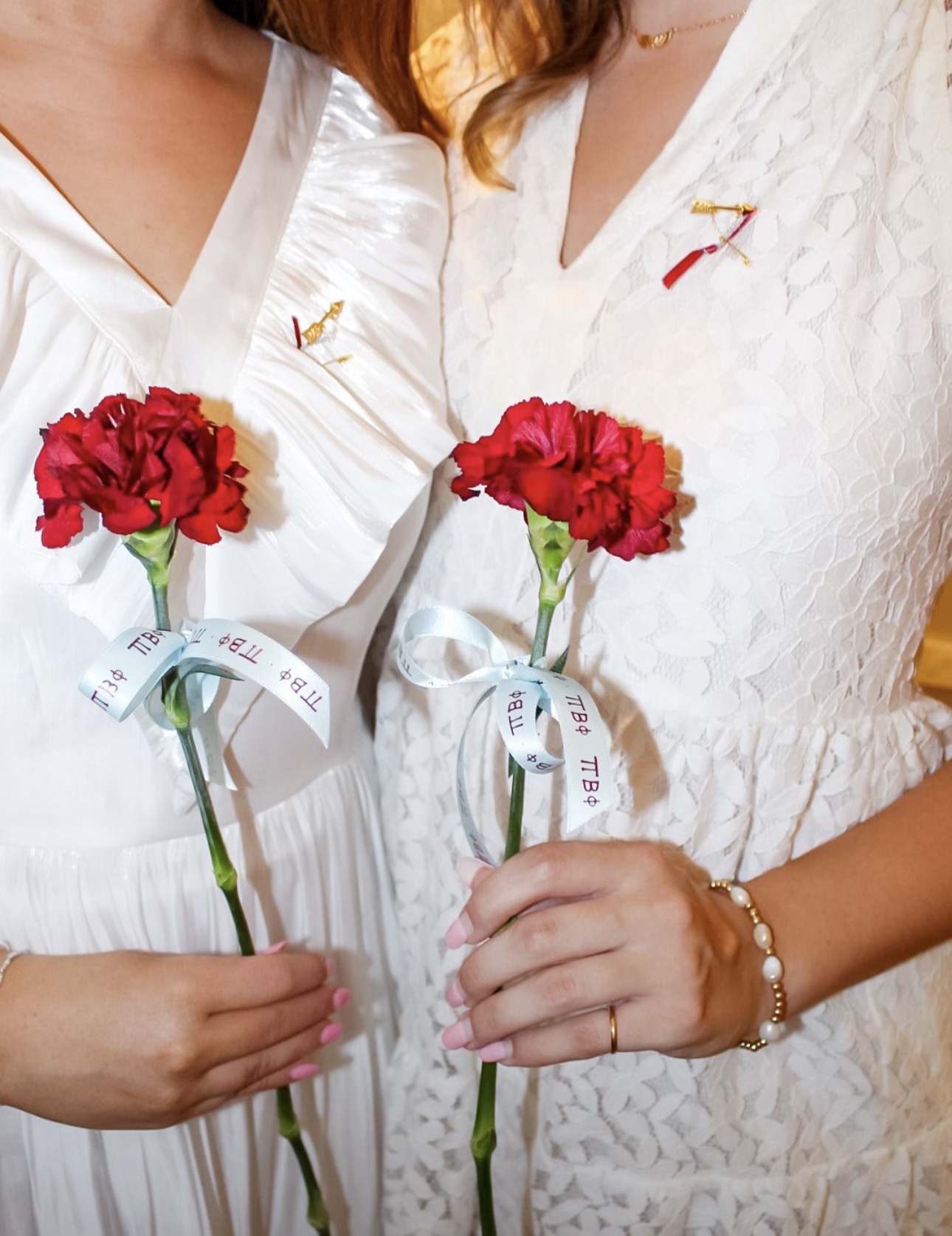 Two members wearing white with their golden arrow badge and wine and silver blue ribbons. they are holding wine carnations tied with a silver blue bow