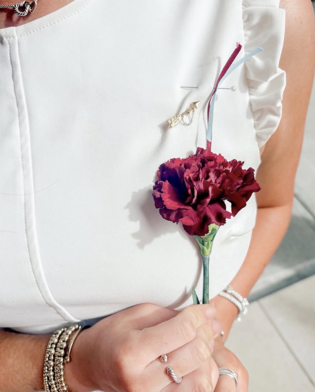 A member wearing a white dress and their arrow badge while holding a wine carnation
