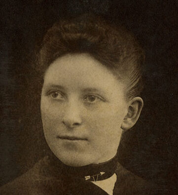 Historical sepia-toned headshot of Elmina Wilson wearing a dark collared shirt in front of a dark background