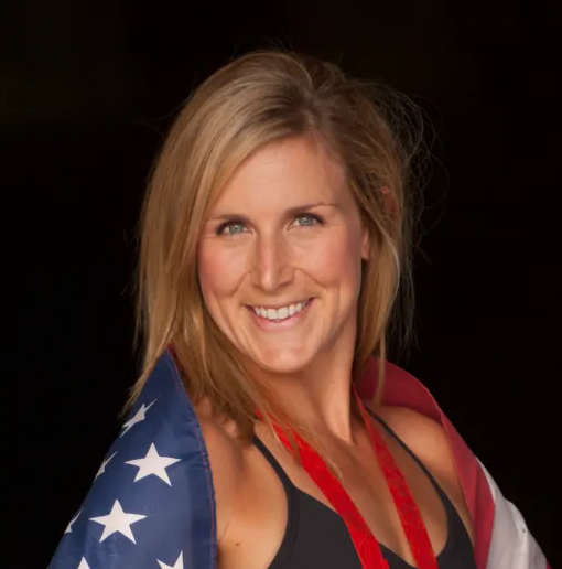 Professional headshot of Erin Jane Cafaro wearing a dark swimsuit top and a red metal strap with an American flag draped over her shoulders