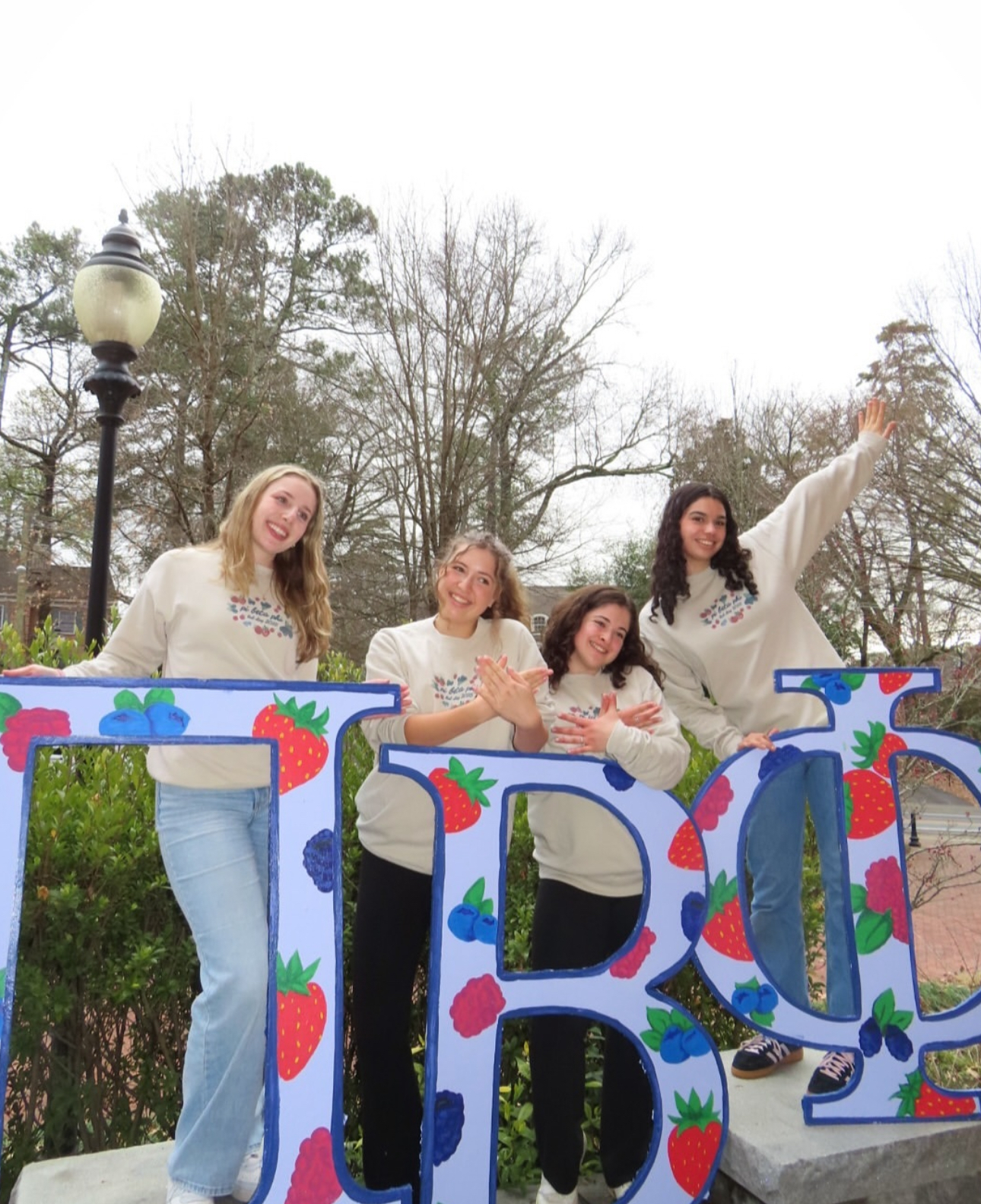 Four individuals standing behind giant Pi Beta Phi Greek letters painted with berries
