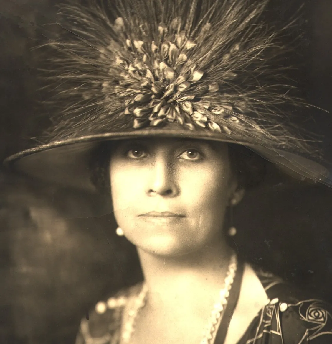 Historical sepia-toned headshot of Grace Goodhue Coolidge wearing a large feathered hat in front of a dark background
